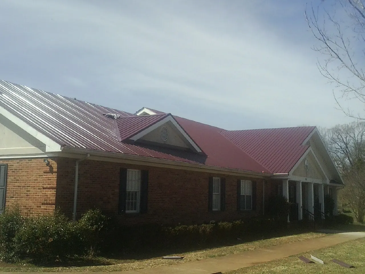Red metal roof with gabled entries on a long brick building, from a Hail Damage Roof Repair job in Chillicothe