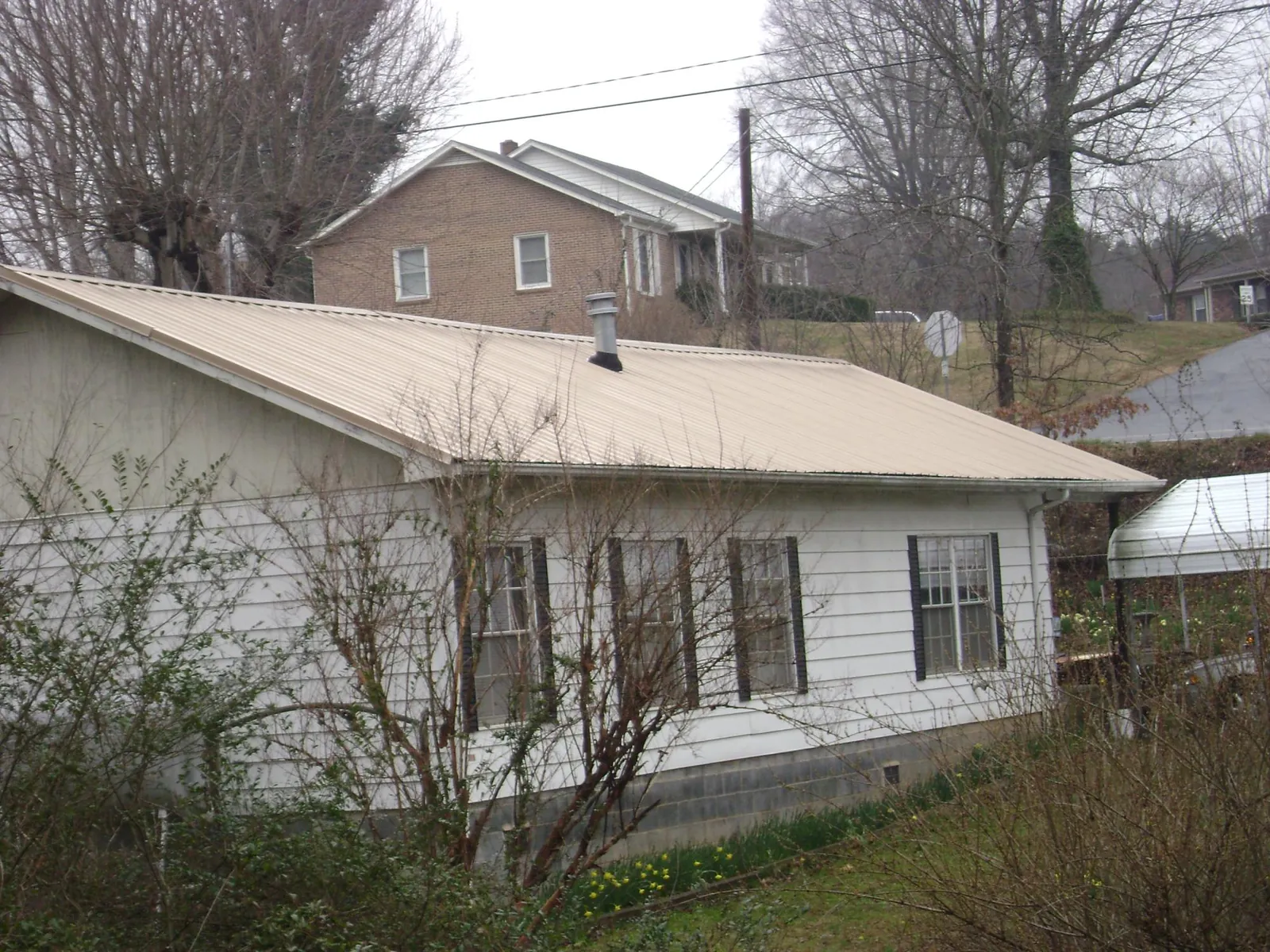 Tan metal roof on a white sided house set into a hillside — Commercial Roofing by Roofing Brothers in Chillicothe